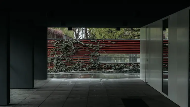 Moderne architektonische Umgebung eines Ausstellungsraums mit rotem Zaun und Kletterpflanzen im Hintergrund.