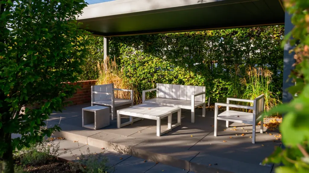 Moderne, überdachte Terrasse mit weißem Outdoor-Möbelset in einer ansprechenden Gartenumgebung.