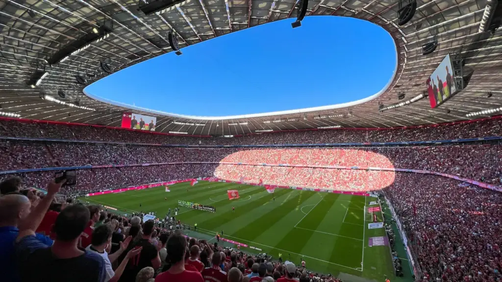 Weites Blickfeld in ein voll besetztes Fußballstadion unter Flutlicht am Spieltag.