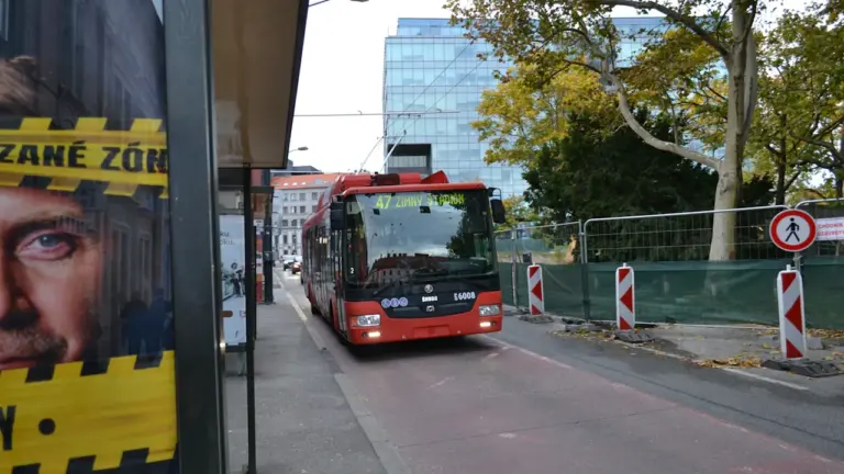 Ein roter Bus wartet an einer Haltestelle in einer städtischen Umgebung.