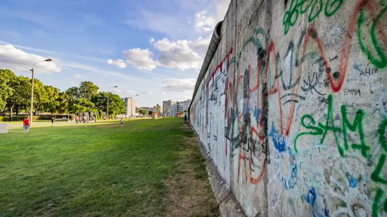 Die Berliner Mauer mit Graffiti trennt eine Grünanlage vom städtischen Raum in Berlin.