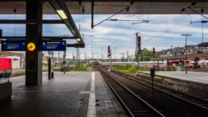 Moderner Bahnsteig mit Gleisen und digitalen Anzeigetafeln an einem Bahnhof.