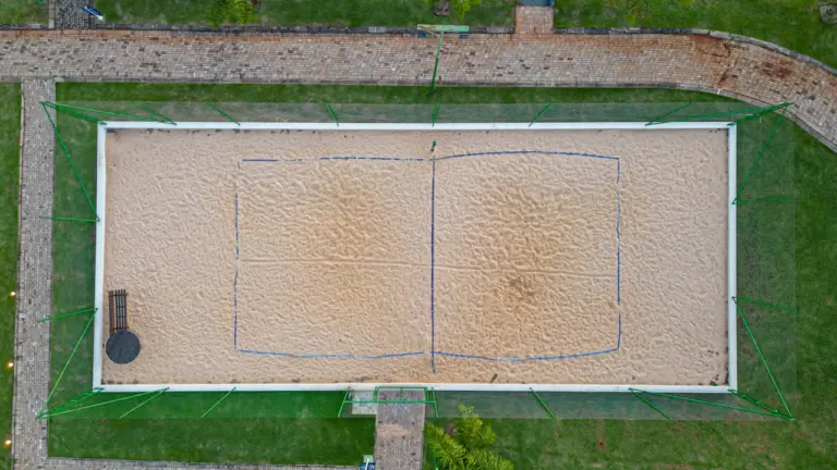 Draufsicht auf ein Beach-Tennis-Spielfeld mit Sandboden in einer Parkanlage.