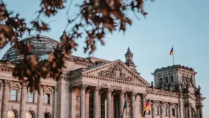 Deutscher Reichstag in Berlin mit wehender Flagge bei strahlend blauem Himmel im Tageslicht.