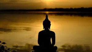 Silhouette einer Buddha-Statue am Wasser bei Sonnenuntergang für eine meditative Stimmung.