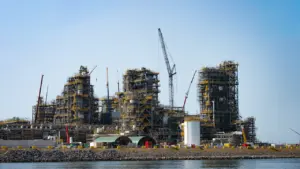 Große Industrieanlage im Bau mit Kränen in einem deutschen Hafen bei sonnigem Wetter.
