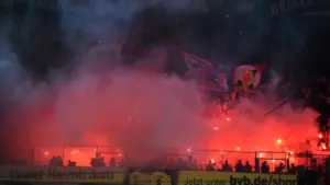 Fußballfans in einem Stadion mit bengalischem Feuer und emotionaler Stimmung.