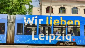 Eine blaue Straßenbahn mit der Aufschrift 'Wir lieben Leipzig' fährt durch die Stadt.