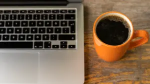 Ein Laptop und eine Tasse Kaffee auf einem Holztisch im Büro.
