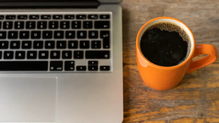 Ein Laptop und eine Tasse Kaffee auf einem Holztisch im Büro.