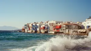 Malerische Küstenstadt am Mittelmeer mit weißen Gebäuden und krachenden Wellen bei strahlendem Sonnenschein.