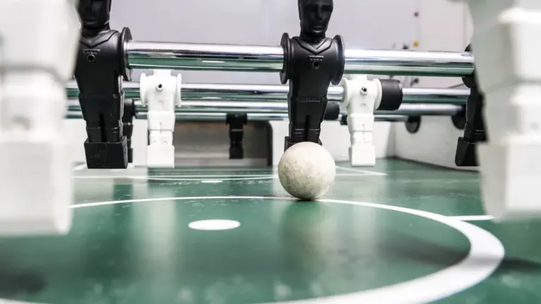Detailansicht eines Tischkickers mit Spielfiguren und einem kleinen Ball auf grünem Feld.