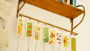 Mehrere handgemachte Lesezeichen mit floralen Motiven hängen an einer hölzernen Wandleiste.