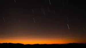 Eine stimmungsvolle Silhouette eines Hügels unter einem nächtlichen Sternenhimmel mit sichtbaren Lichtspuren von Sternschnuppen.