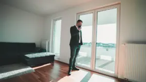 Ein Mann im Anzug steht an einer Balkontür und telefoniert in einer hellen Wohnung.