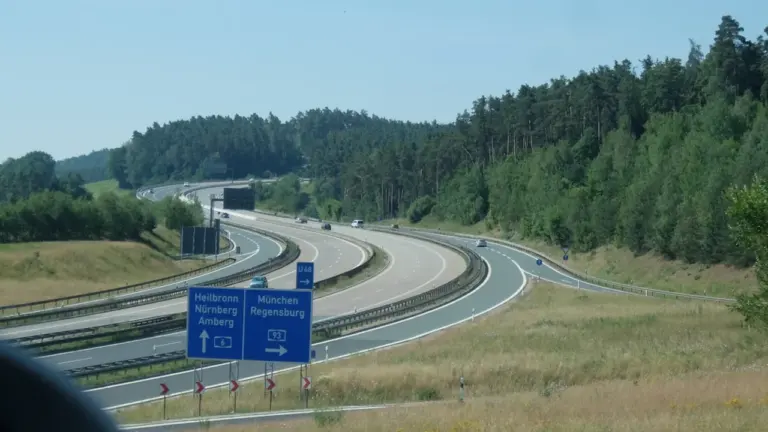 Autobahn mit Hinweisschildern in Richtung Regensburg umgeben von einem grünen Waldgebiet.
