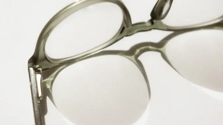 Nahaufnahme einer Brille mit hellgrünem Rahmen, die einen Schatten auf eine weiße Fläche wirft.