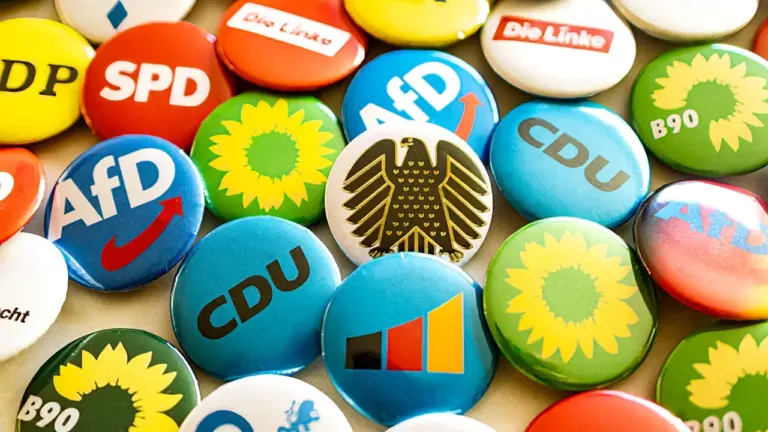 Verschiedene Ansteckbuttons deutscher politischer Parteien liegen auf einem Tisch verteilt.