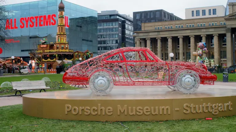 Rote Porsche-Drahtskulptur vor dem Haus der Geschichte in Stuttgart bei Tageslicht.