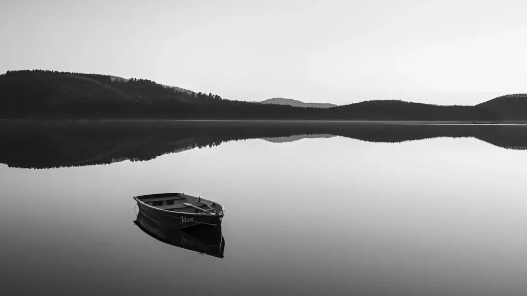 Ein einsames Boot auf einem ruhigen See vor einer Berglandschaft.