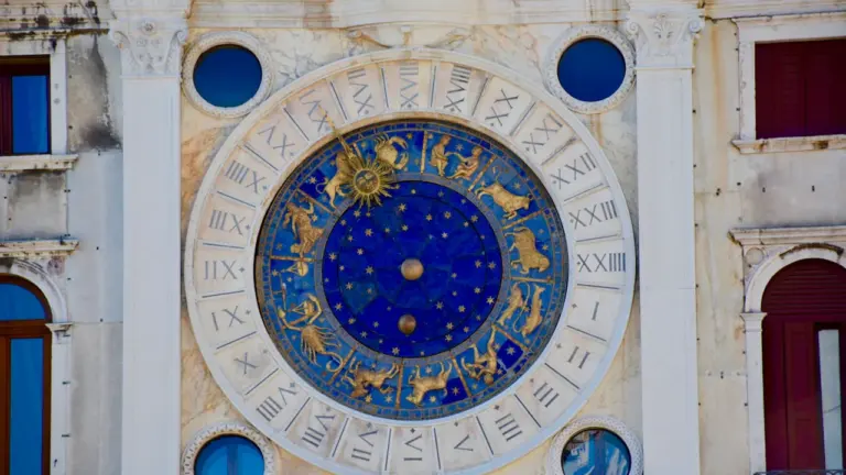 Detailaufnahme einer historischen astronomischen Uhr mit goldenen Sternzeichen auf blauem Hintergrund.