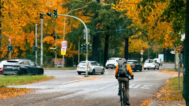 Ein Radfahrer fährt auf einer herbstlichen Straße in Berlin entlang einer belebten Kreuzung.