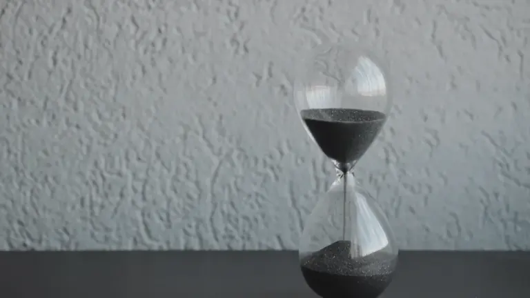 Eine Sanduhr mit blauem Sand am Strand, symbolisch für vergängliche Zeit und Achtsamkeit.