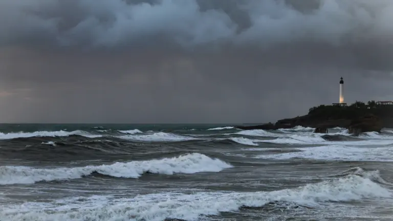 Ein Leuchtturm an einer felsigen Küste bei aufgewühlter, stürmischer See und dunklen Wolken.
