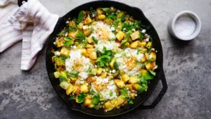 Gusseiserne Pfanne mit gebratenem Gemüse, Feta und frischen Kräutern servierbereit.
