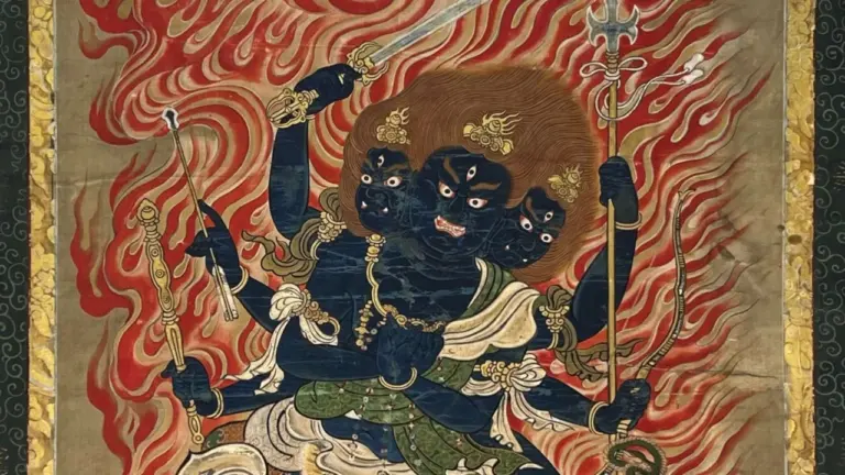 Eine dreiköpfige, dunkelblaue buddhistische Gottheit mit sechs Armen vor einem flammenden roten Hintergrund.