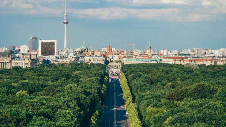 Luftaufnahme vom Berliner Fernsehturm über der grünen Parklandschaft des Tiergartens bei blauem Himmel.