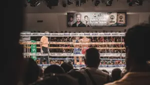 Zwei Boxer stehen sich im Boxring vor einem begeisterten Publikum in einer Arena gegenüber.