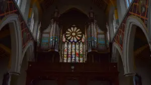 Prächtige Kirchenorgel vor einem kunstvollen bunten Glasfenster in einer Kirche.