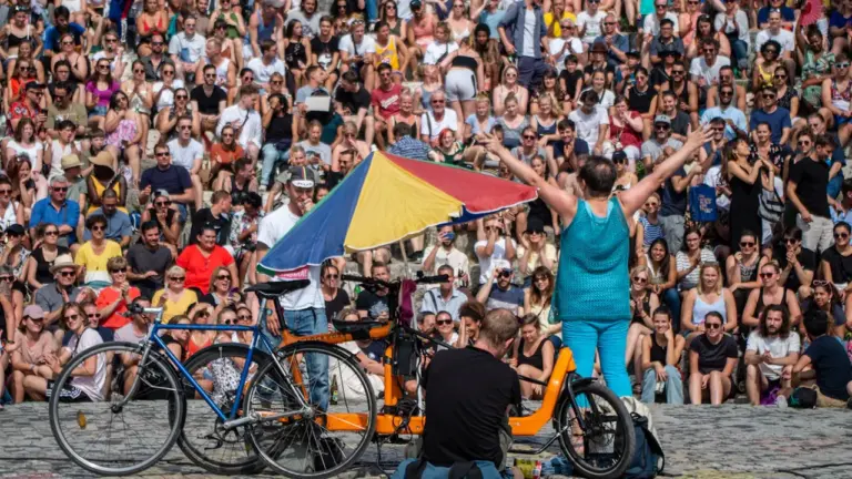 Menschenmenge im Freien bei einer Straßenaufführung mit Fahrrad und Sonnenschirm in Paderborn