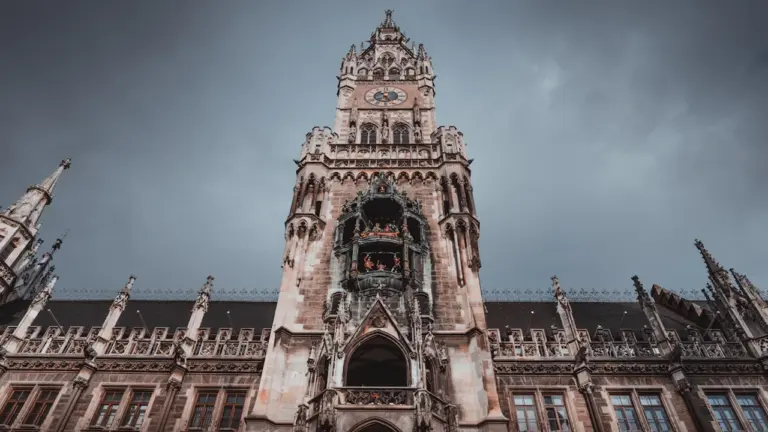 Das beeindruckende Neue Rathaus am Marienplatz in München unter einem dramatischen, bewölkten Himmel.