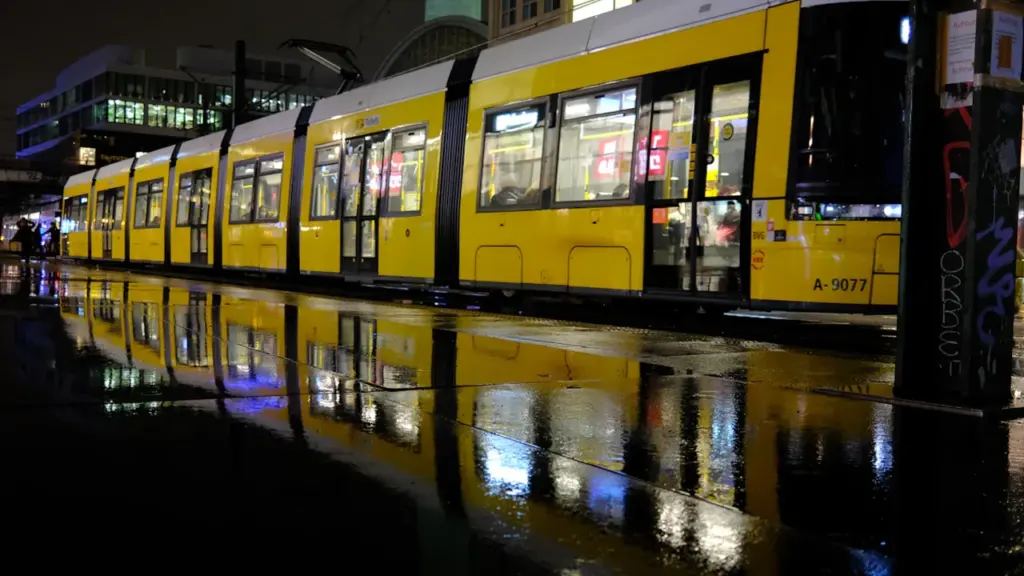 Eine gelbe Berliner Straßenbahn bei Nacht auf nassen Gleisen in der Stadt.