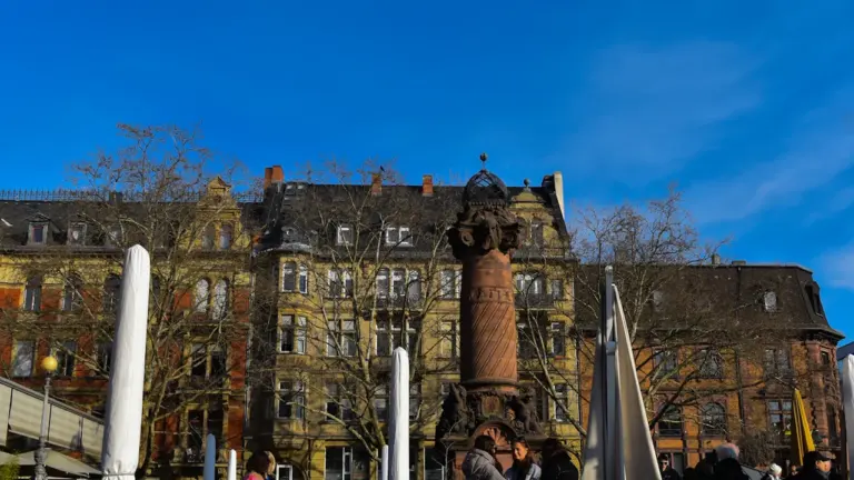 Menschen sitzen auf einer Bank vor historischer Architektur auf einem belebten Stadtplatz.