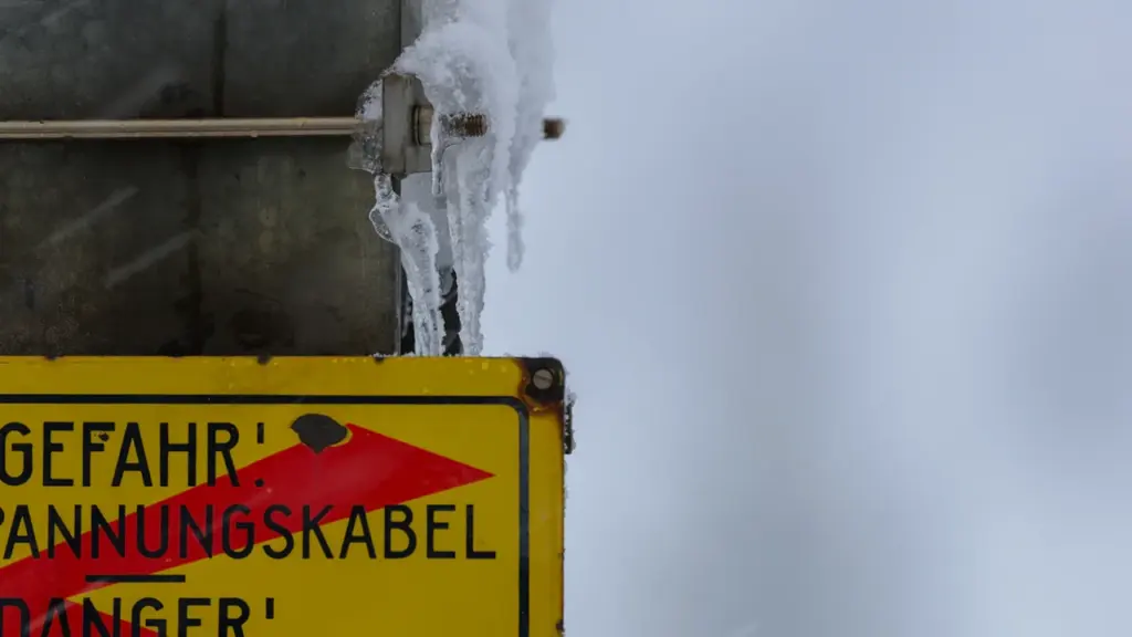 Ein gelbes Warnschild mit Eiszapfen unter einem trüben, winterlichen Himmel in Deutschland.