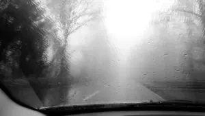 Regentropfen auf der Windschutzscheibe eines Autos auf einer nebligen Straße bei schlechtem Wetter